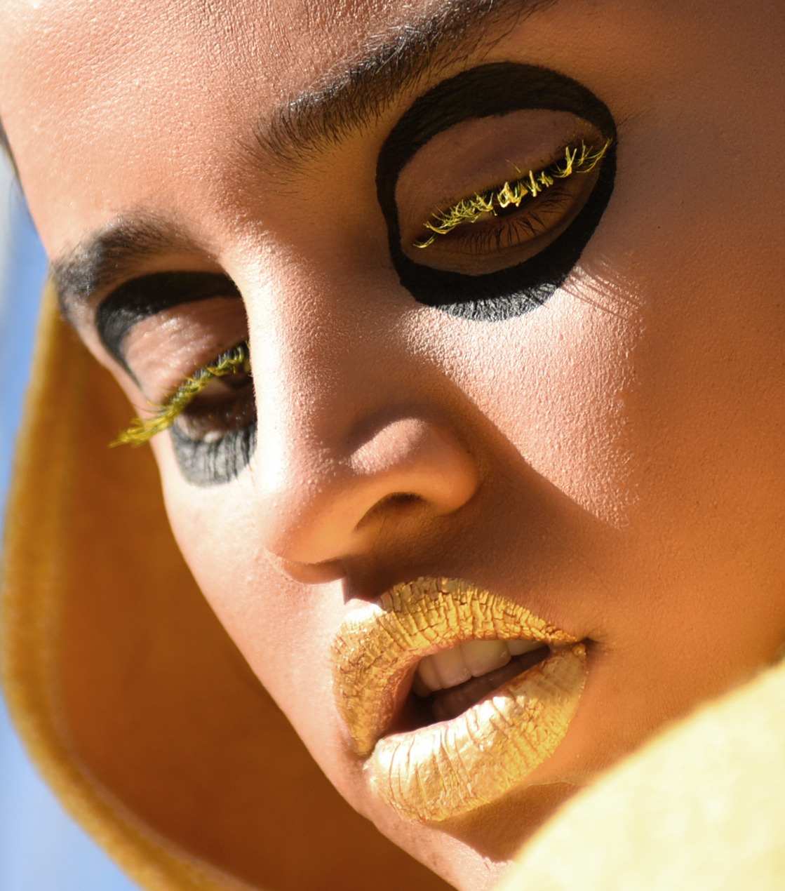 Close-up beauty shot with gold lips and bold graphic eye make-up