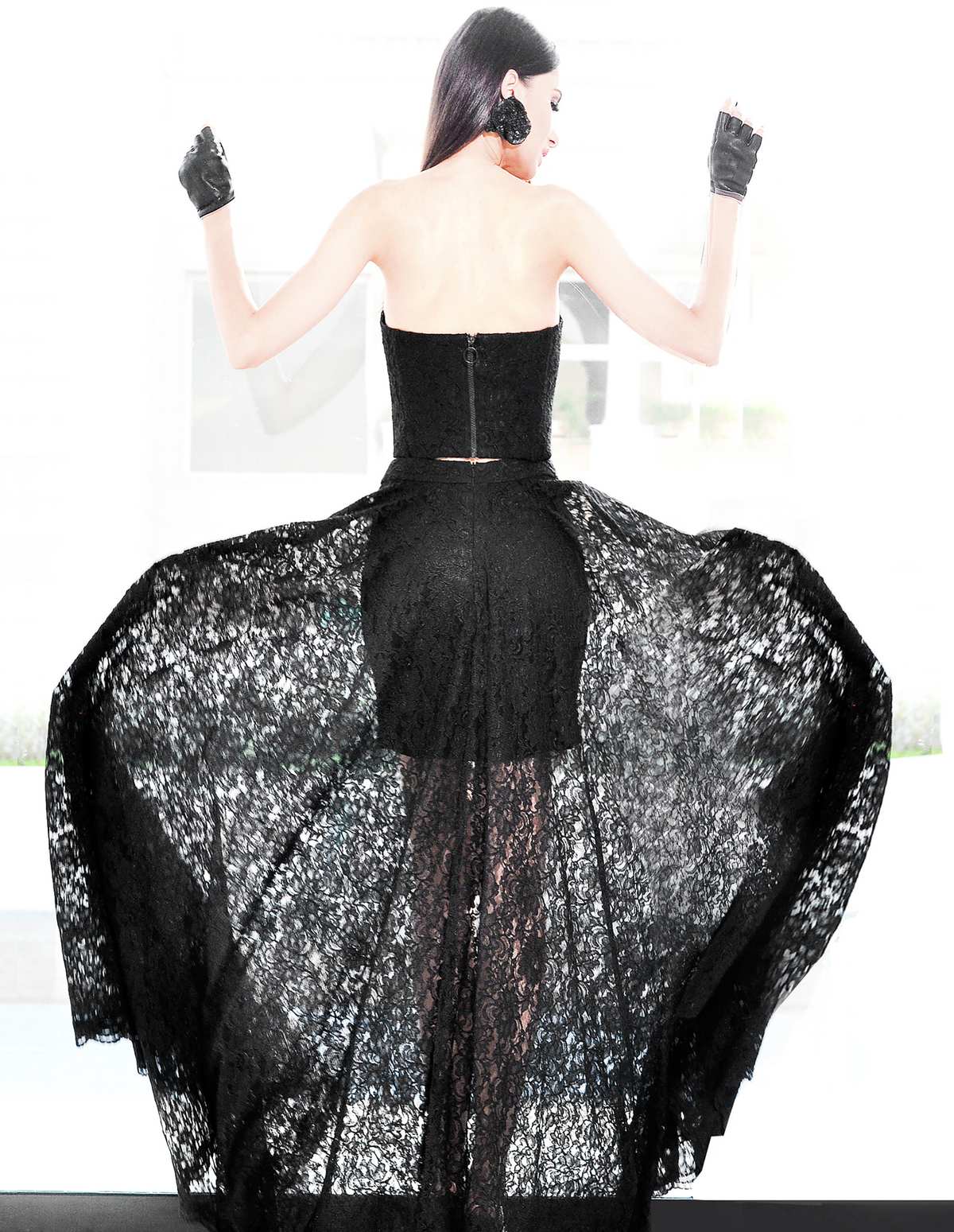 A woman seen from behind in a black lace gown, arms raised