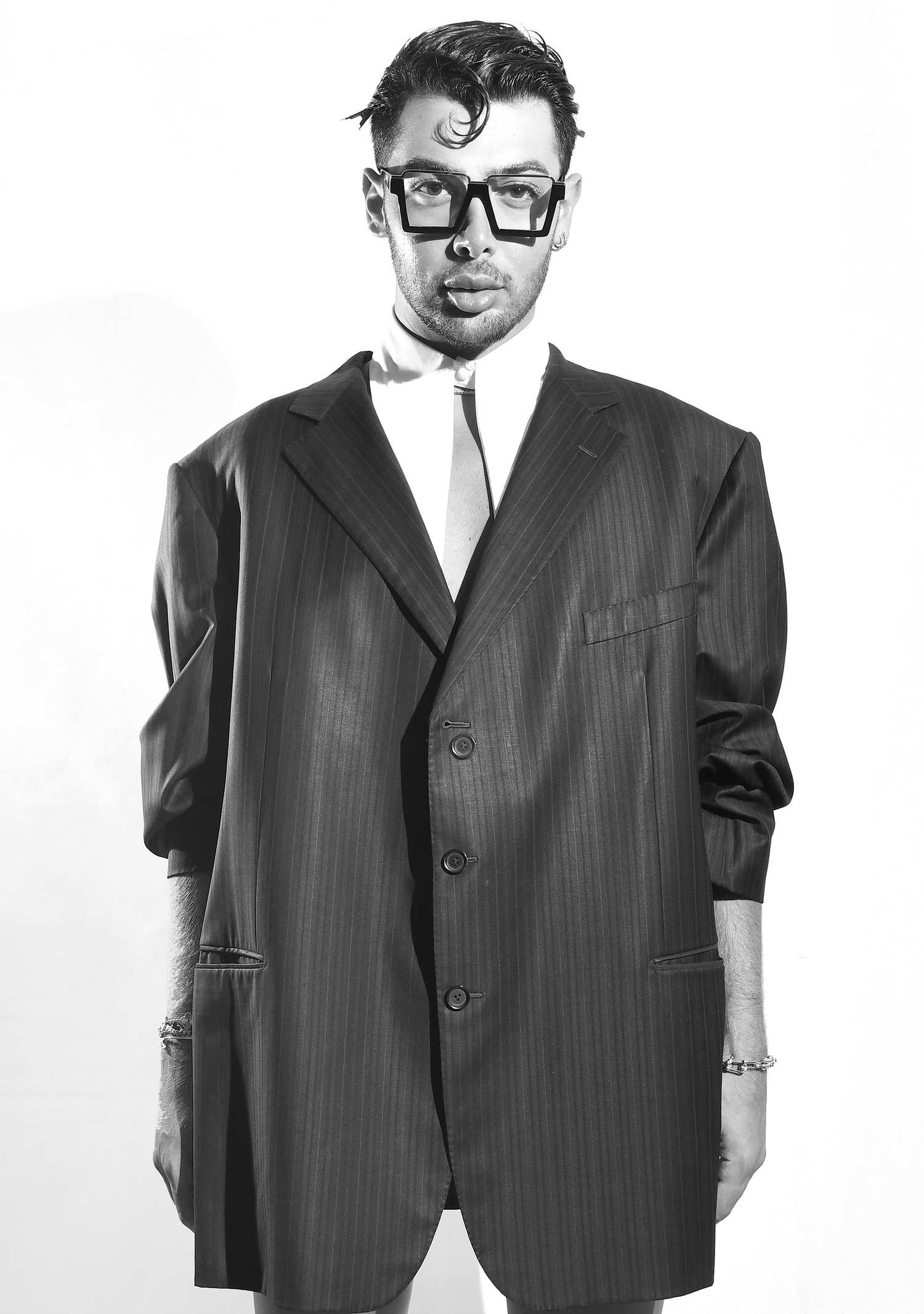 Black and white portrait of a man in an oversized pinstripe suit and square glasses