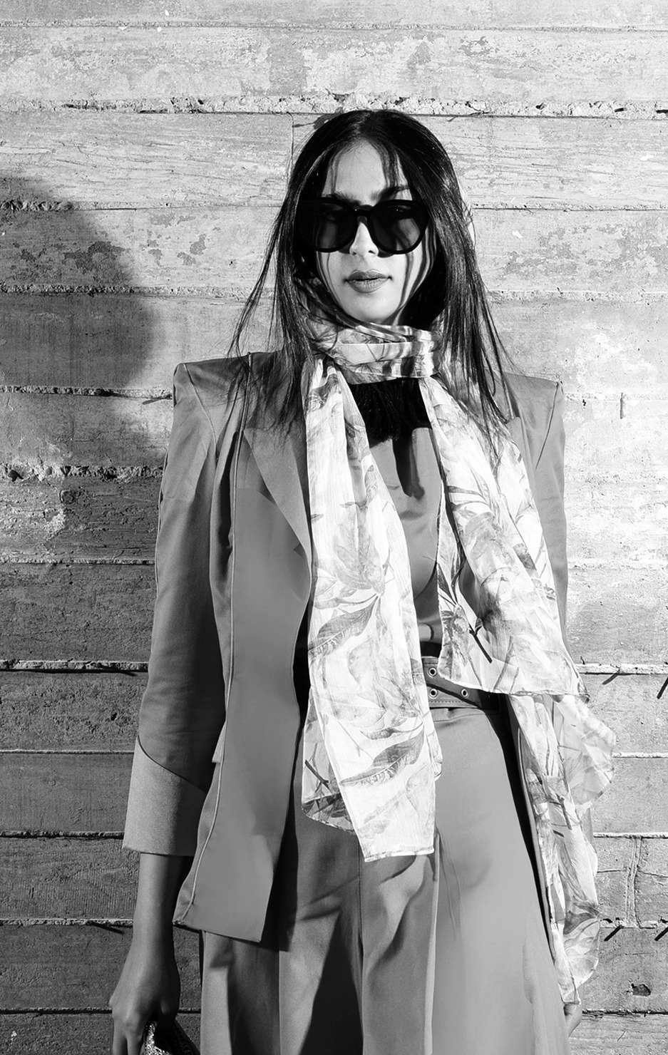 Black and white fashion portrait of a woman in sunglasses, a silk scarf and a tailored jacket